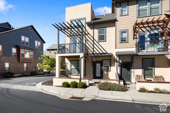 Multi-level townhome featuring a stucco and siding exterior, multiple balconies with pergolas, and an inviting front entrance with an overhang