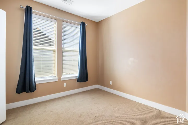 Neutral tone walls and carpeting, featuring two windows with horizontal blinds