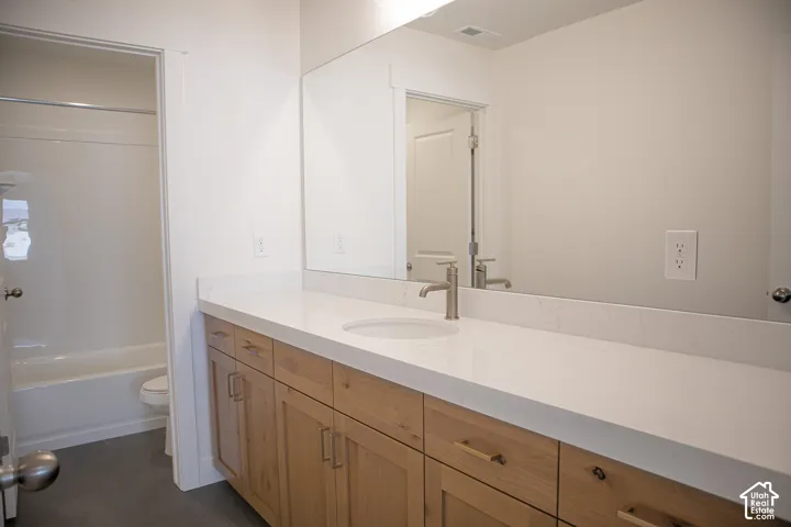 Full secondary bath with extra-long vanity, stained wood cabinets, quartz slab countertops and door between vanity and shower.