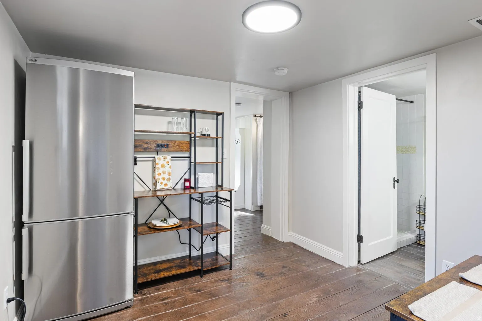 Stainless steel refrigerator, warm wood-finish flooring, recessed ceiling light, and a white panel door
