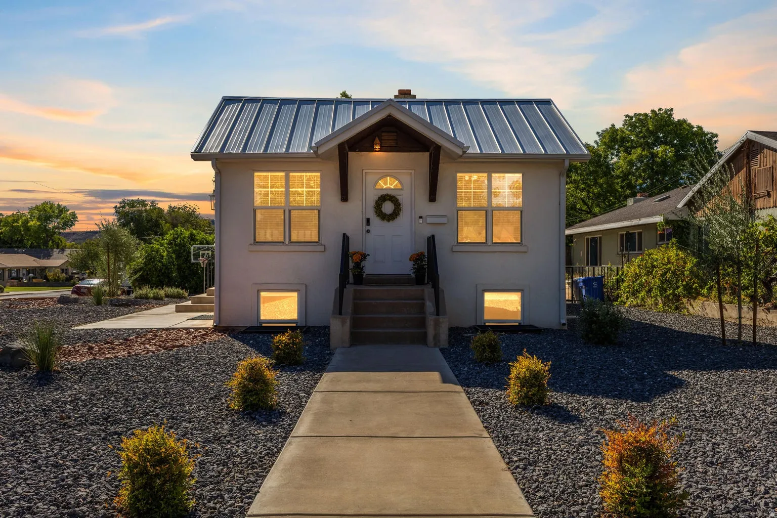Stucco exterior with a metal roof, concrete walkway, and gravel landscaping