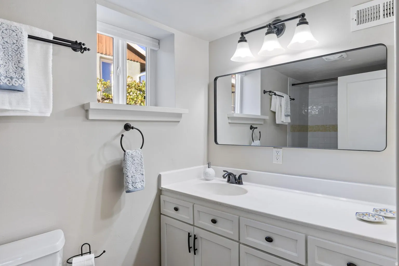 White shaker-style vanity with dark hardware, a single basin sink, and a spacious countertop