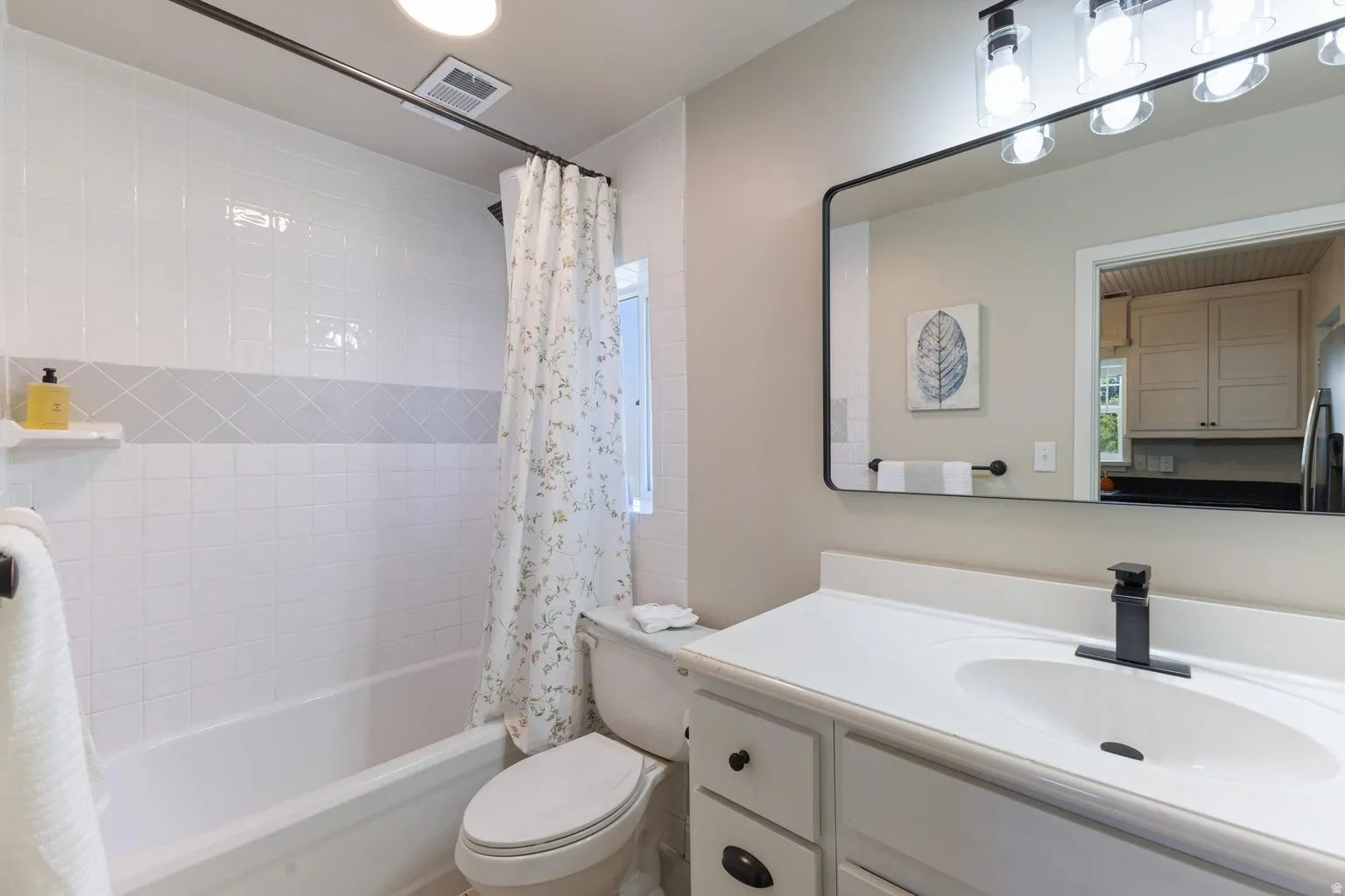 Bathroom featuring a white subway tile surround with a decorative accent band, a white vanity with integrated sink, a matte black faucet, a large rectangular mirror, and an overhead light fixture