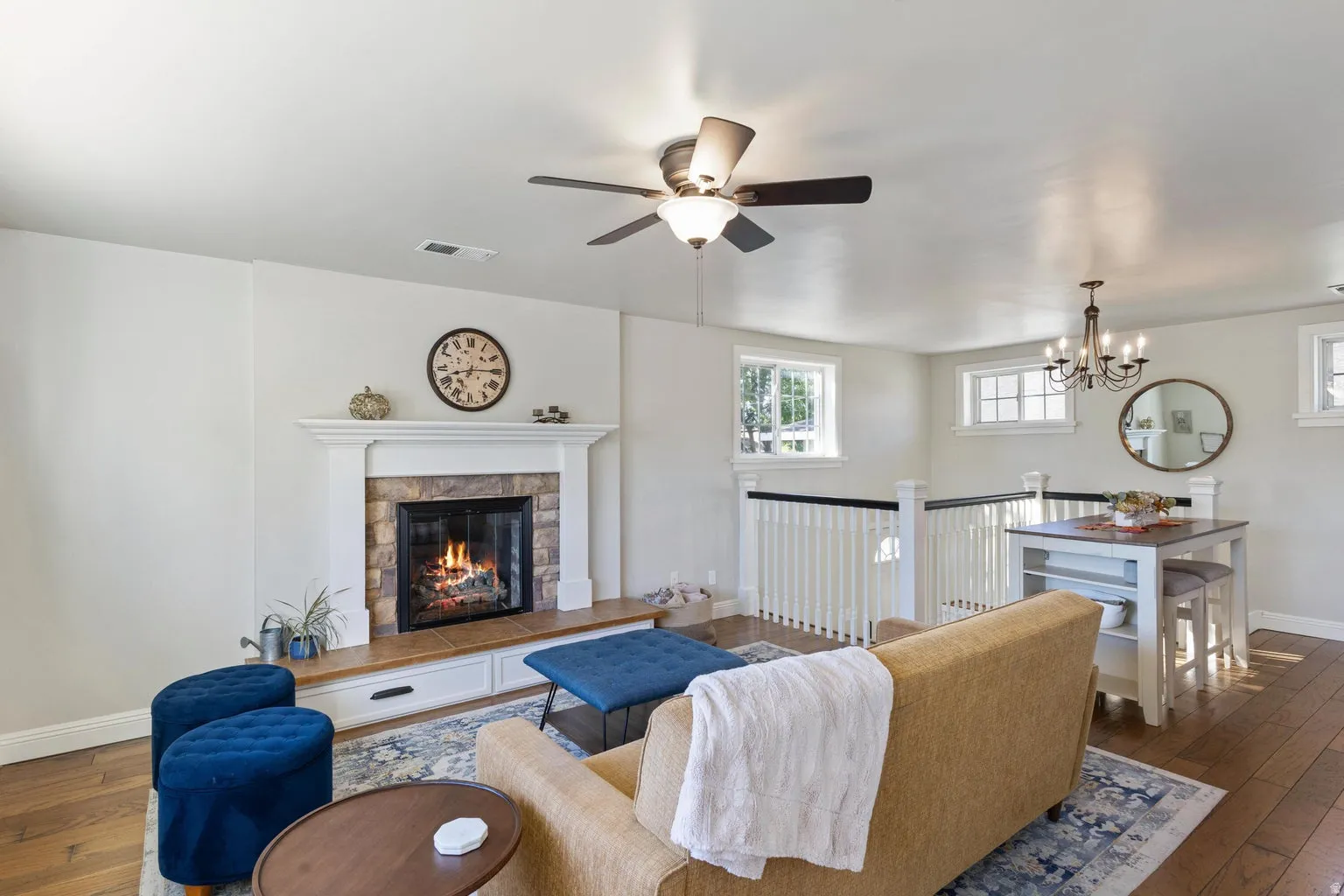 Fireplace with stone surround and mantle, wood-finish flooring, built-in storage, and ceiling fan with integrated lighting