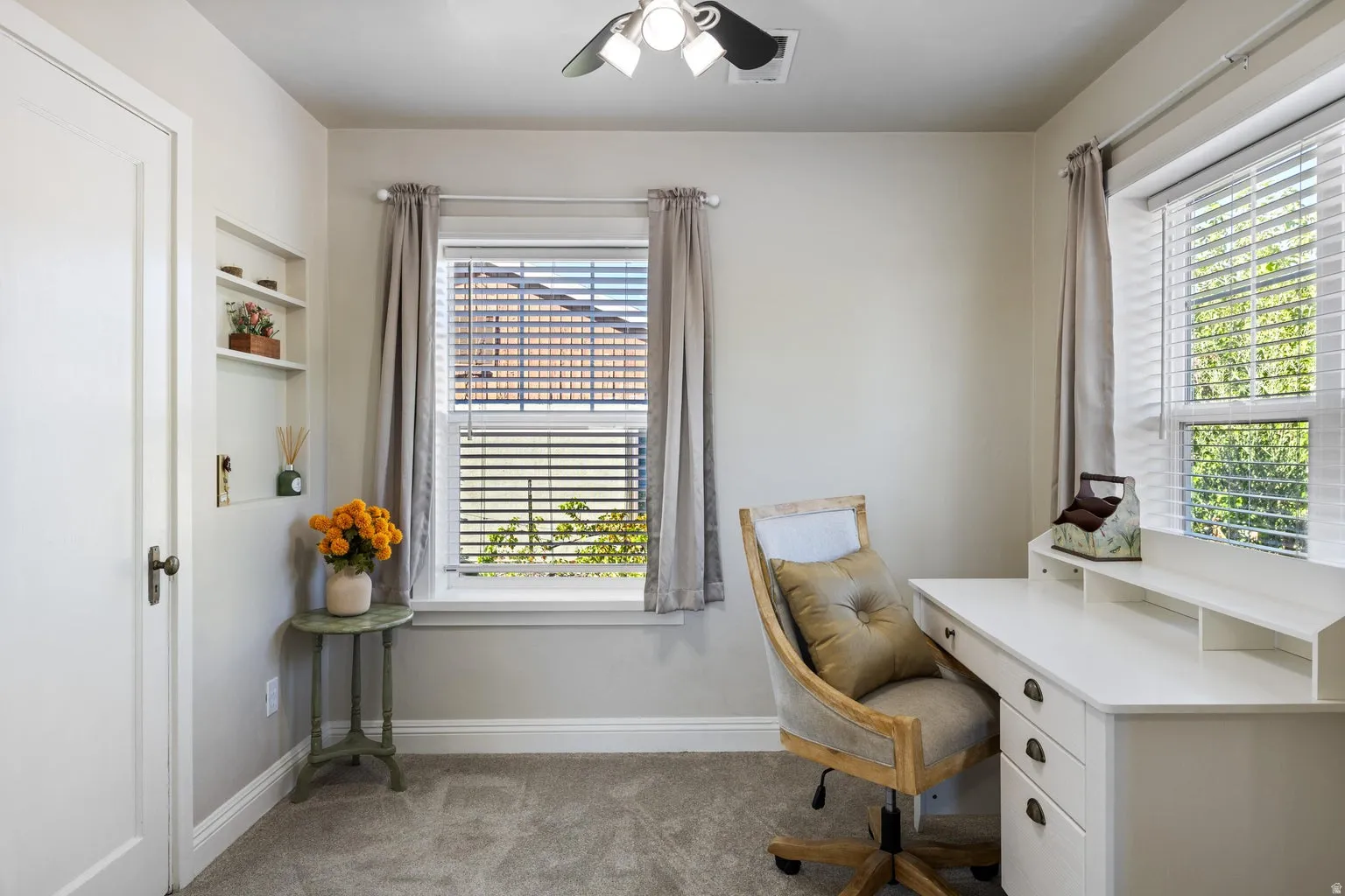 Built-in shelving, window with blinds and drapes, ceiling fan, and light-toned wall paint