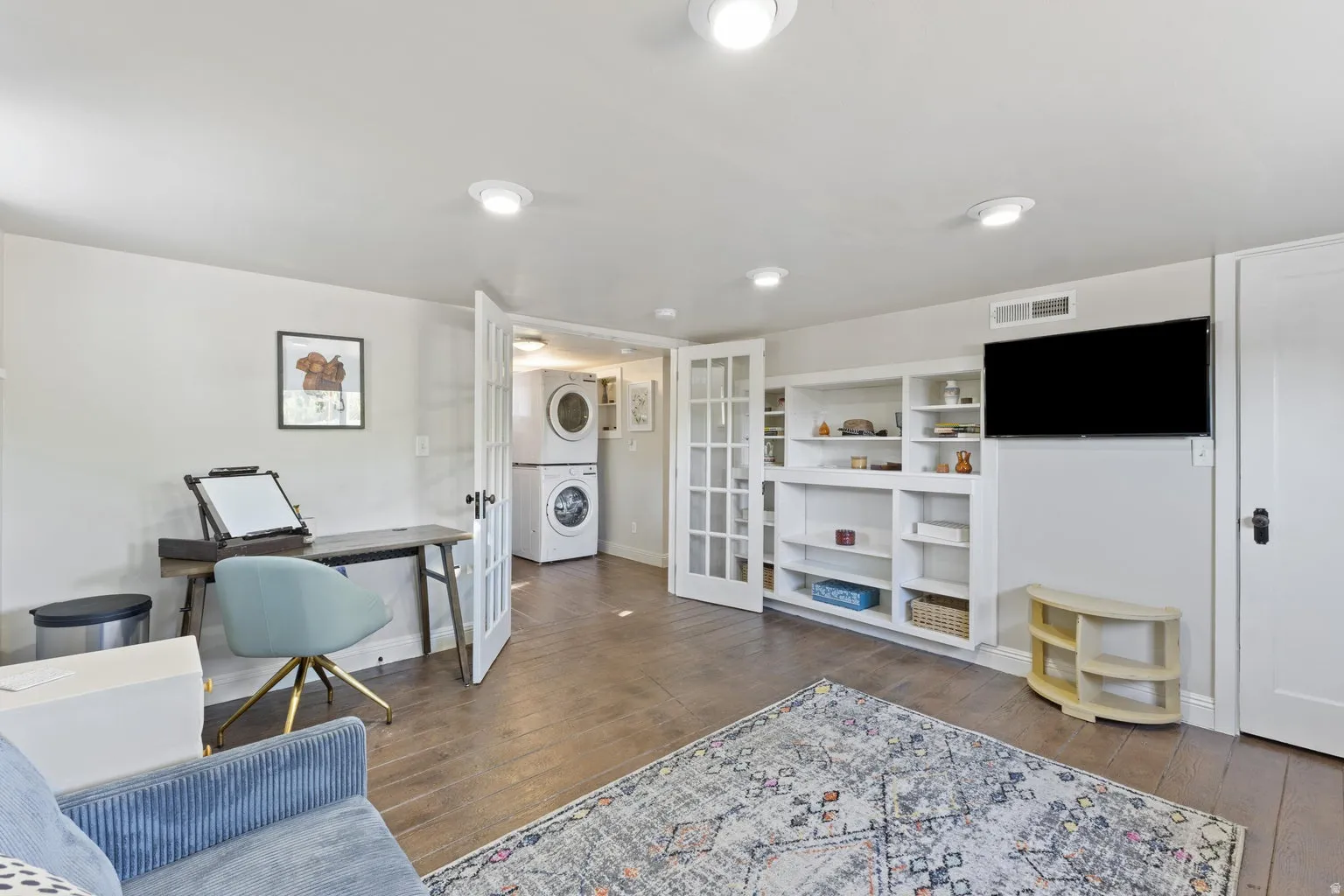Recessed lighting throughout, wood-finish flooring, built-in shelving, French doors, and a laundry area with stacked appliances