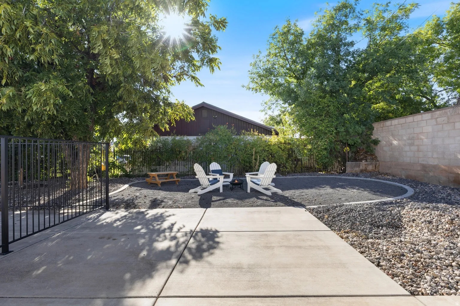 Paved patio area with a fenced perimeter, featuring a circular gravel fire pit zone, and a block wall border