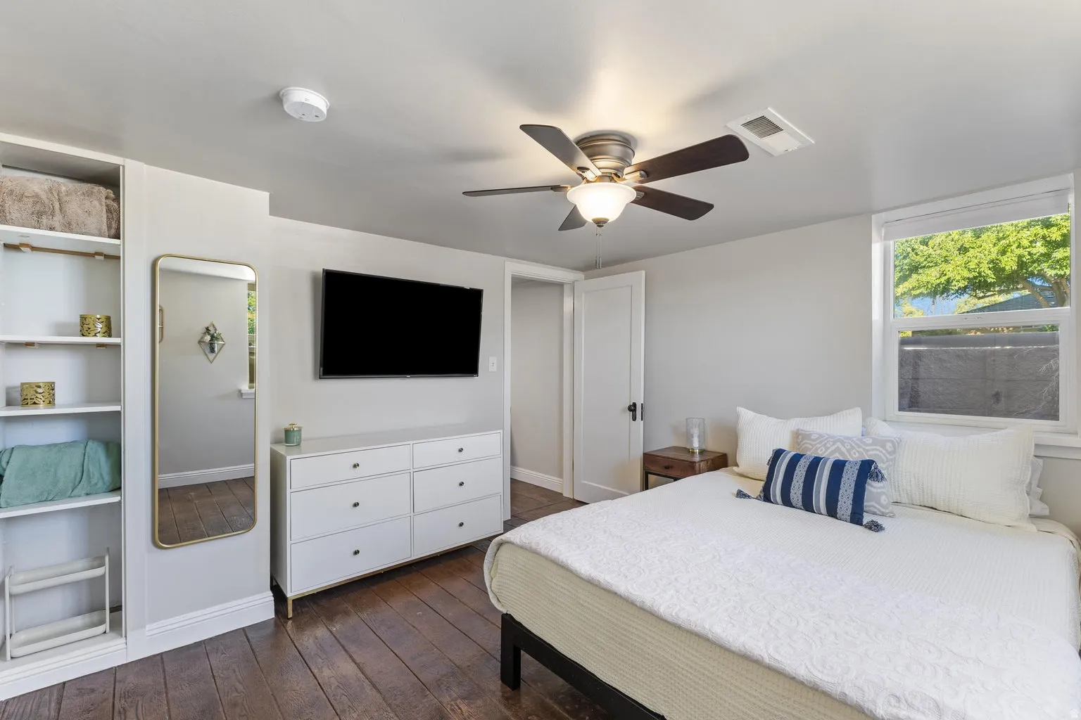Hardwood flooring, built-in shelving, white trim, ceiling fan with integrated lighting, and a double-hung window
