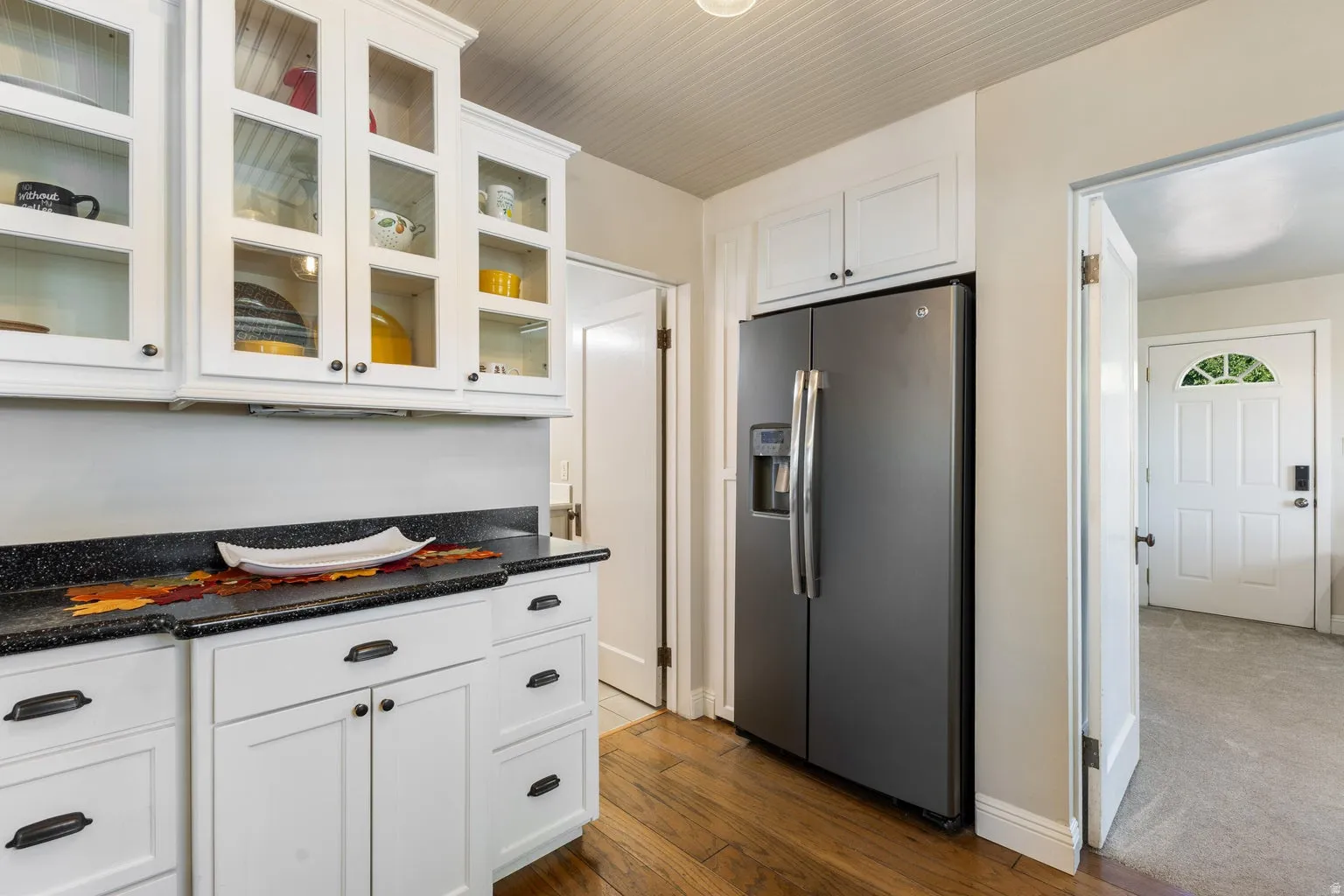 White cabinetry with glass-front upper doors, dark speckled countertops, and wood-finish flooring