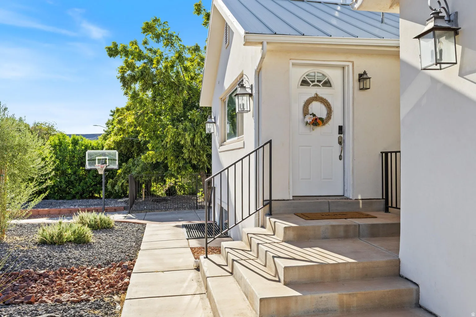 White exterior with a metal roof, concrete steps, wrought iron handrails, and a white entry door with a transom window