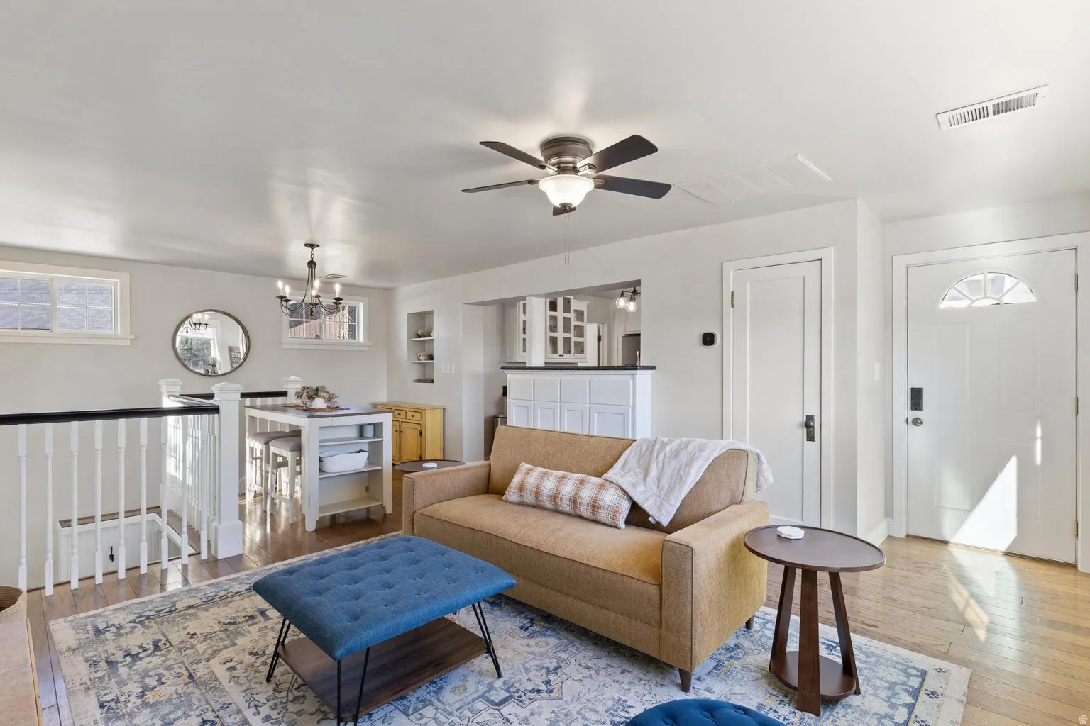 Bright living area featuring wood-finish flooring, a ceiling fan with integrated lighting, and a white paneled door with an arched transom