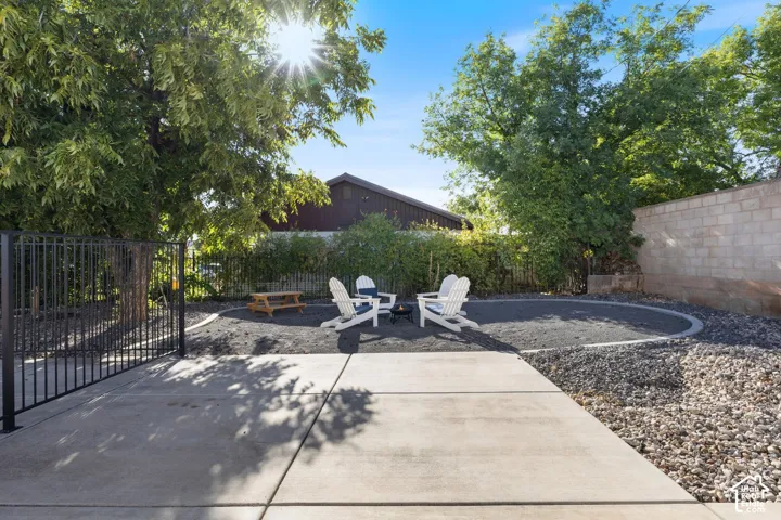 Paved patio area with a fenced perimeter, featuring a circular gravel fire pit zone, and a block wall border