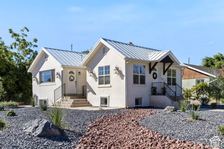 Stucco exterior featuring dual entryways with metal roofs, exterior sconce lighting, and a xeriscaped front yard with decorative rock and plantings