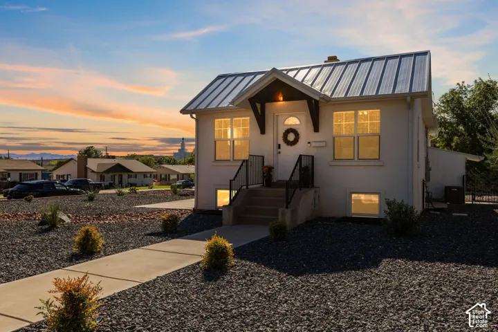 White exterior with a metal roof, prominent entry porch, concrete walkway, and gravel landscaping