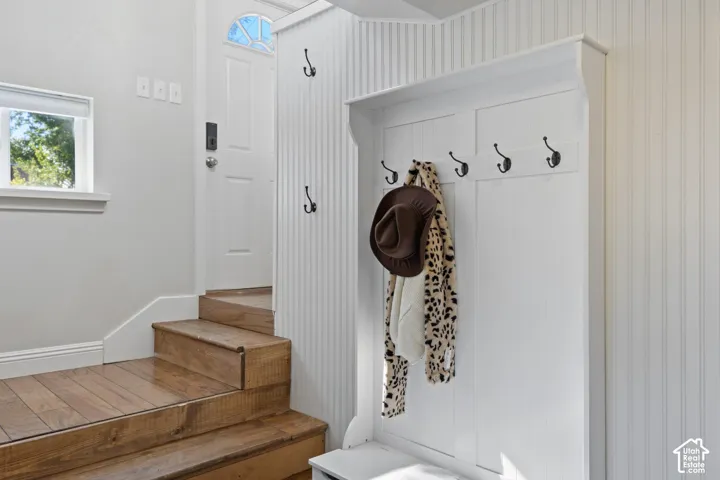 Entryway featuring wood-finish stairs, a white paneled door with an arched transom, a built-in white coat rack with black hooks, and white beadboard wall paneling