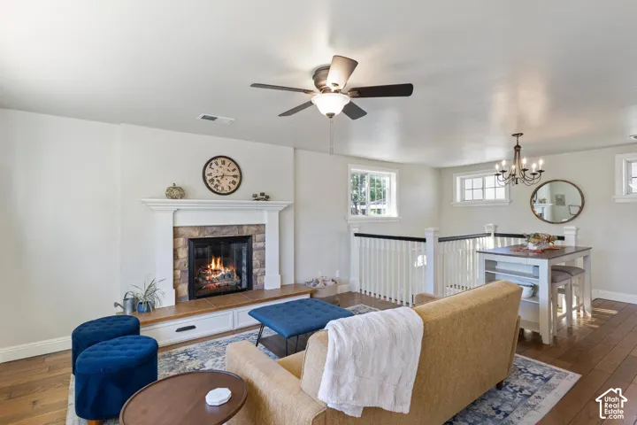 Fireplace with stone surround and mantle, wood-finish flooring, built-in storage, and ceiling fan with integrated lighting