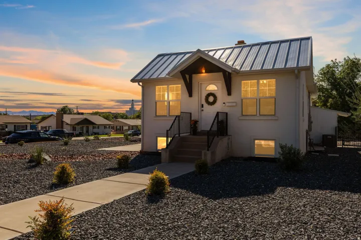 White exterior with a metal roof, prominent entry porch, concrete walkway, and gravel landscaping