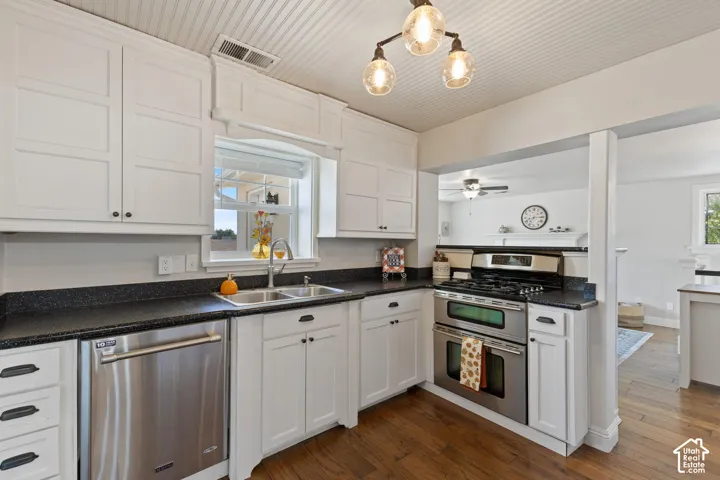 White shaker-style cabinetry with dark hardware, stainless steel appliances, dark countertops, a double basin sink, and wood-finish flooring
