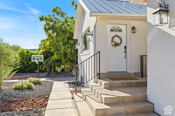 White exterior with a metal roof, concrete steps, wrought iron handrails, and a white entry door with a transom window