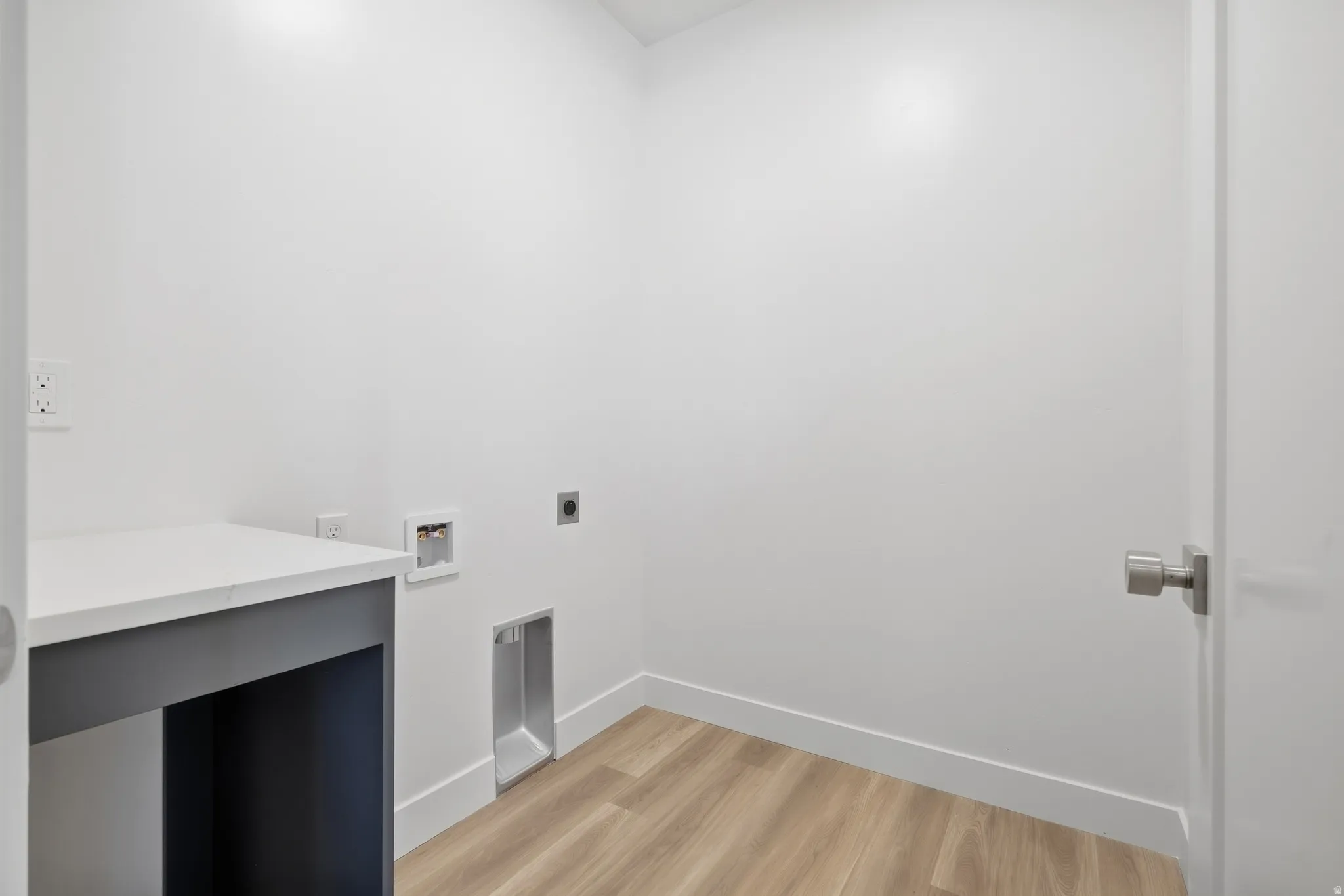 Dedicated laundry area featuring a built-in counter, wood-finish flooring, and a contemporary door with a brushed metal handle