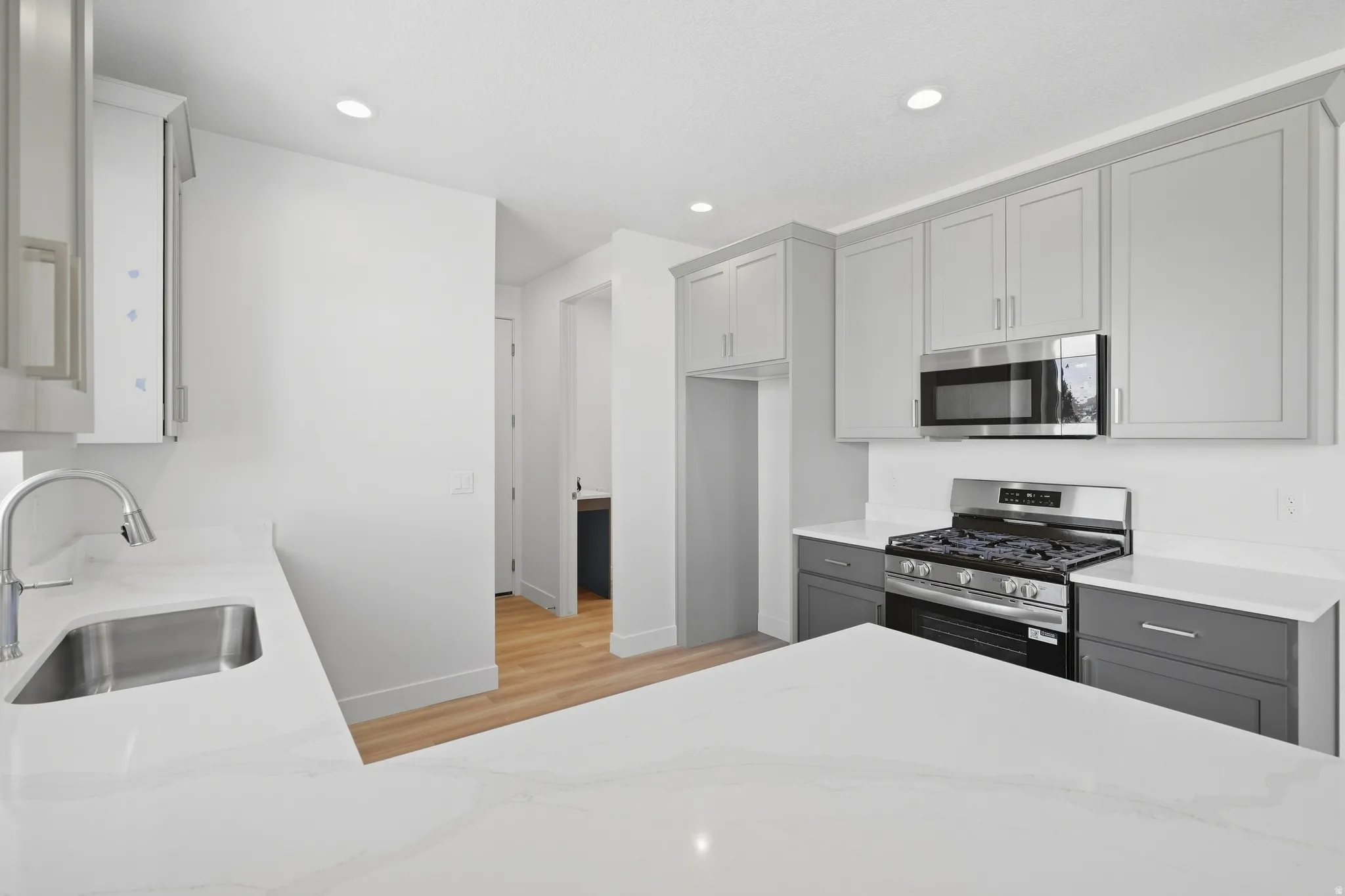 Kitchen featuring light gray upper cabinetry, dark gray lower cabinetry, stainless steel appliances, a stainless steel sink, and light-toned countertops