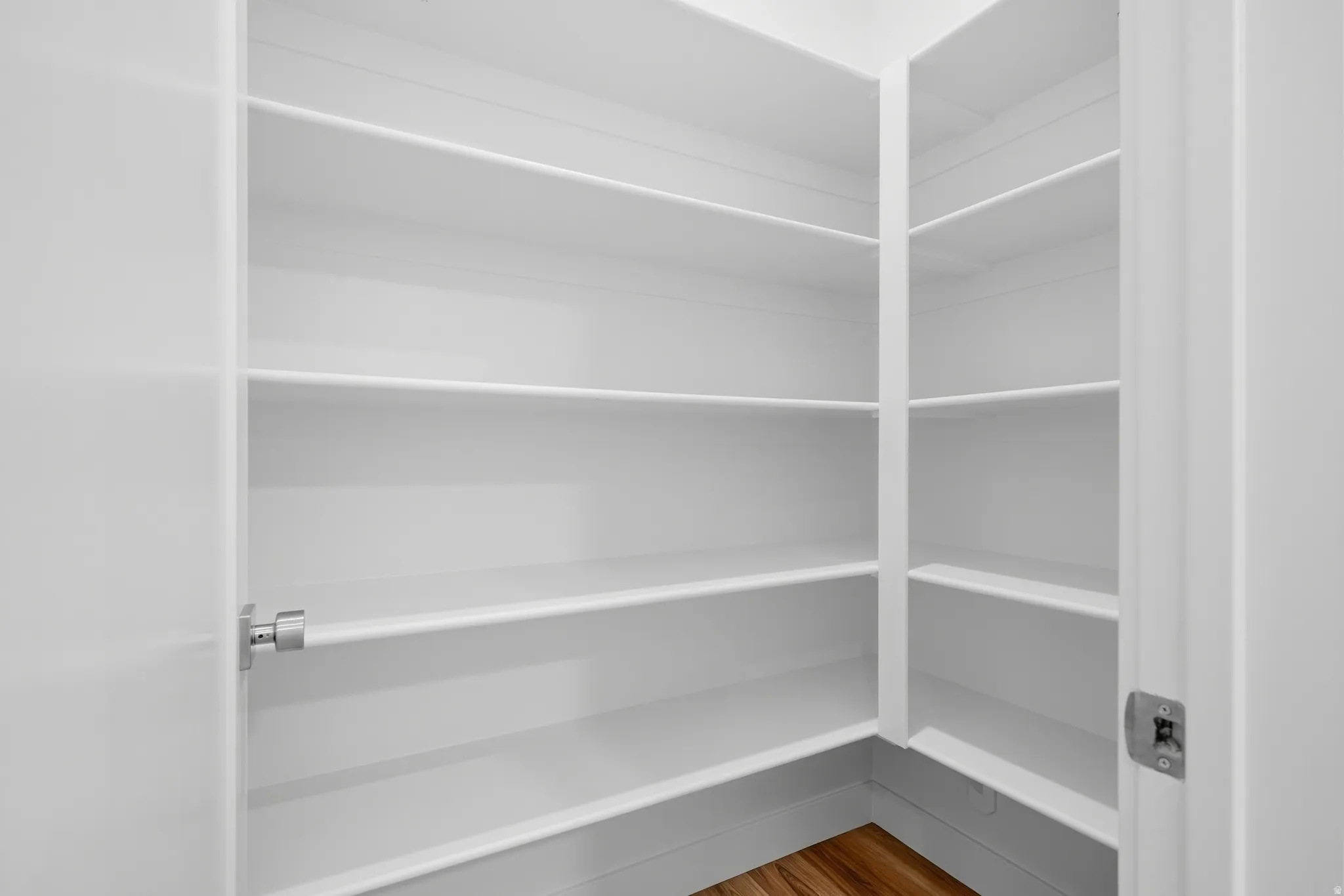 Spacious pantry with multiple white shelving units and wood-finish flooring