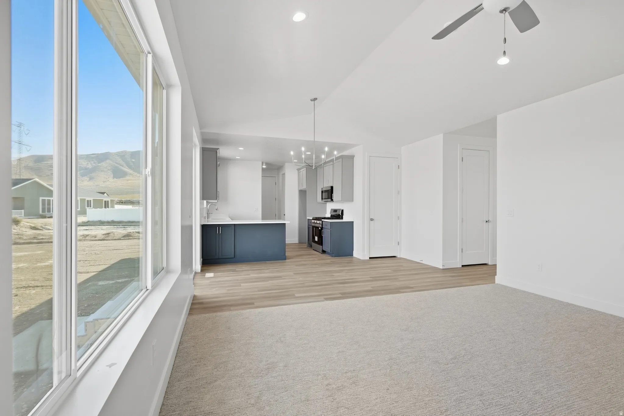 Expansive window wall, recessed lighting, ceiling fan, wood-finish flooring, and a kitchen featuring a peninsula with dark blue cabinetry