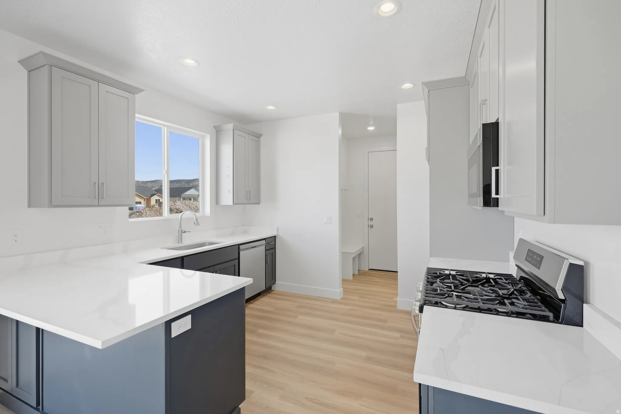 Modern kitchen featuring light gray and dark blue cabinetry, white countertops, stainless steel appliances, and light wood-finish flooring