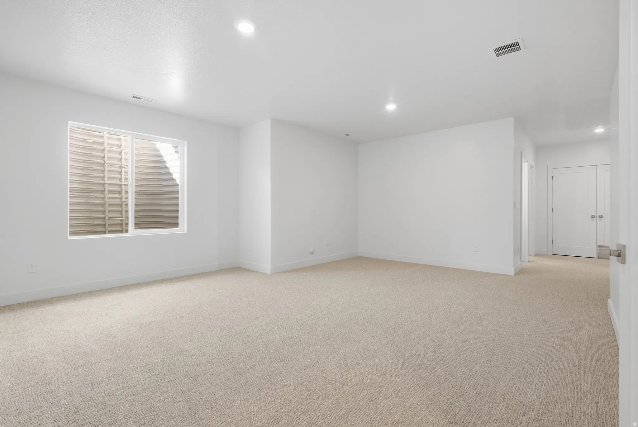Spacious room featuring neutral carpeting, recessed lighting, white walls, and a large window