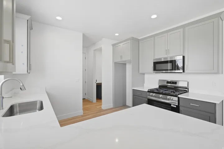 Kitchen featuring light gray upper cabinetry, dark gray lower cabinetry, stainless steel appliances, a stainless steel sink, and light-toned countertops