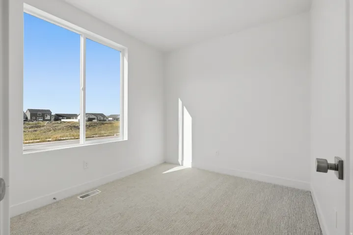 White walls with a single large window, light-colored textured carpeting, and a modern door handle