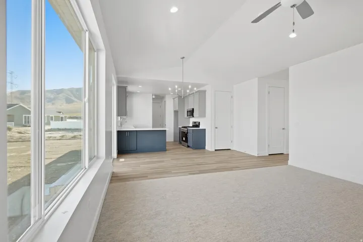 Expansive window wall, recessed lighting, ceiling fan, wood-finish flooring, and a kitchen featuring a peninsula with dark blue cabinetry