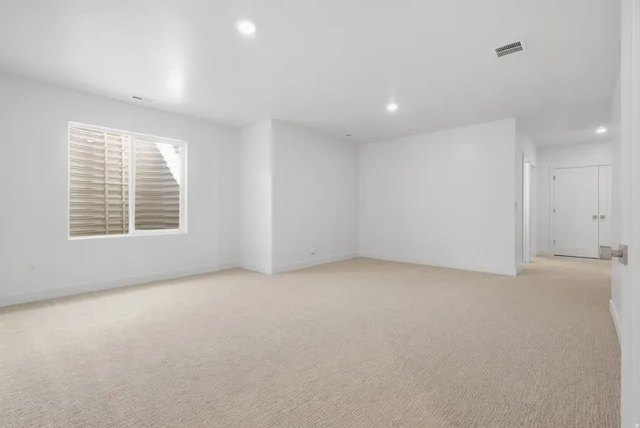 Spacious room featuring neutral carpeting, recessed lighting, white walls, and a large window