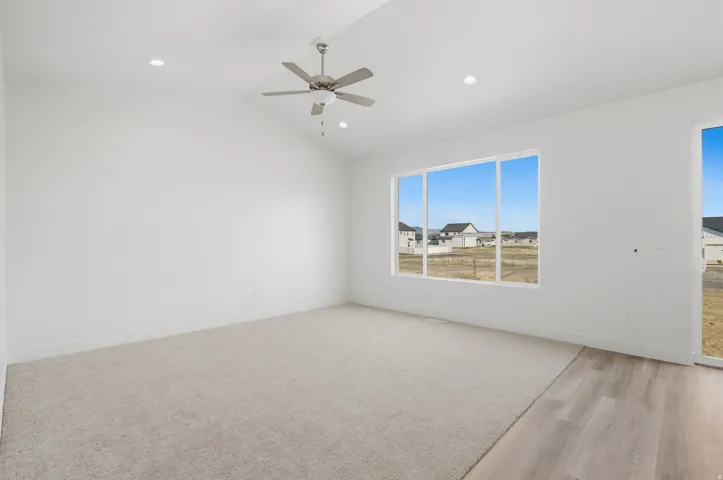 Vaulted ceiling featuring a ceiling fan and recessed lighting, light-toned carpeting, wood-finish flooring, and expansive windows