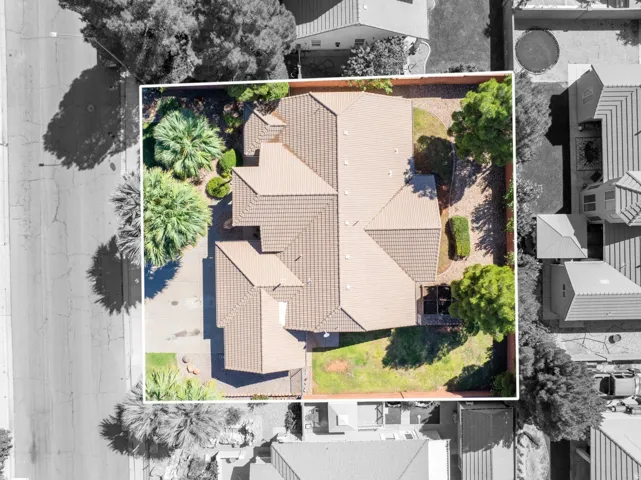 Terracotta tile roof with multiple gables, paved driveway, mature landscaping, and a fenced backyard with grass and trees