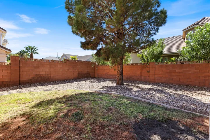 Enclosed backyard featuring a mature tree, a full-height block wall, and stone ground cover