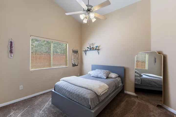 Vaulted ceiling with ceiling fan, large window with horizontal blinds, neutral wall tones, and carpeted flooring