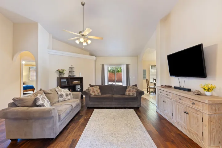 Vaulted ceilings, wood-finish flooring, ceiling fan with integrated lighting, arched doorways, and sliding glass door