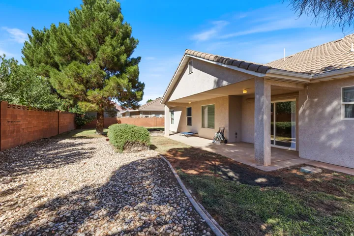 Expansive backyard featuring a covered patio, xeriscaping, mature trees, and a block fence