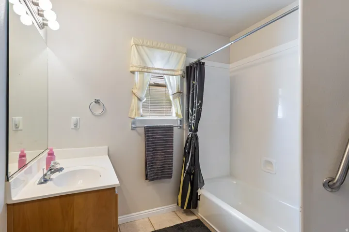 White built-in bathtub with shower, wood-finish vanity with countertop and integrated sink, wall-mounted mirror, and overhead vanity lighting