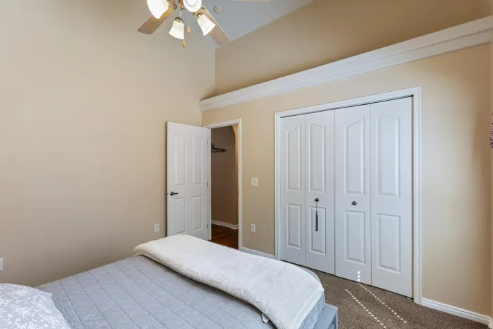 Vaulted ceiling with an attached ceiling fan, crown molding, double bi-fold closet doors, and wood-finish flooring