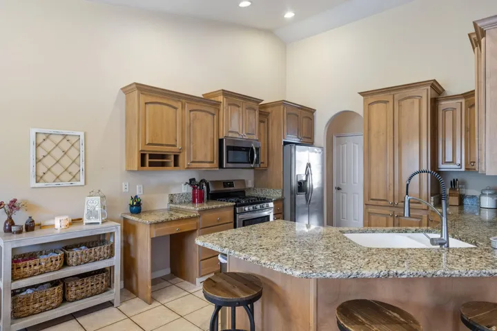 Kitchen featuring abundant wood cabinetry, granite countertops, stainless steel appliances, a built-in kitchen desk, and an undermount sink with a high-arc faucet