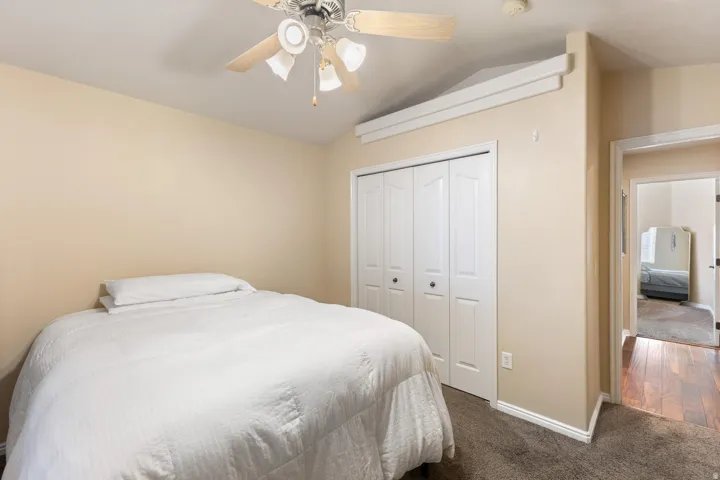 Vaulted ceiling, ceiling fan with light kit, bi-fold closet doors, wall-to-wall carpeting, and wood-finish flooring in the hallway