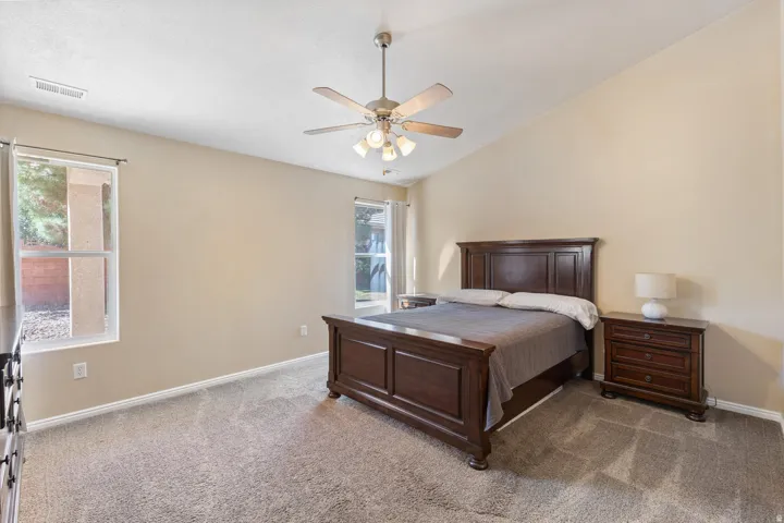 Vaulted ceiling, ceiling fan with integrated lighting, two windows, and carpet flooring