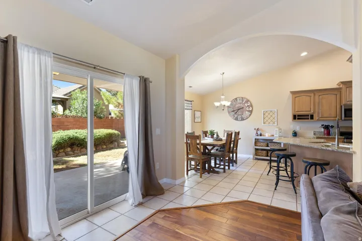 Sliding glass doors to the exterior patio, vaulted ceiling, arched doorway, kitchen island with breakfast bar seating, and wood-finish flooring