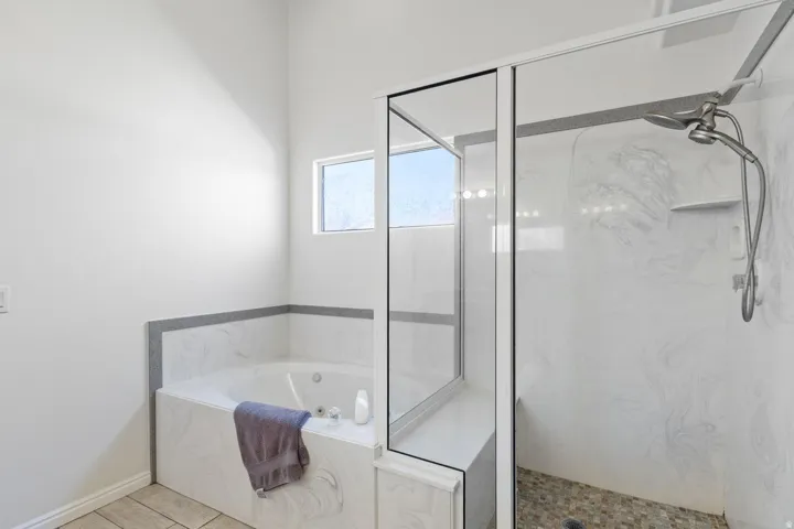 Built-in bathtub with tiled surround, adjacent to a glass-enclosed shower with a multi-function shower head, and tile flooring
