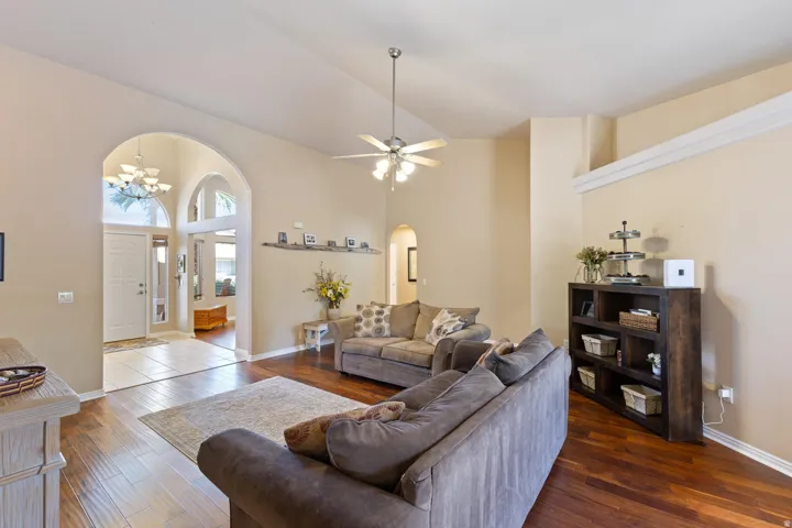 Vaulted ceiling, ceiling fan with light fixture, wood-finish flooring, arched entryway, and tile flooring