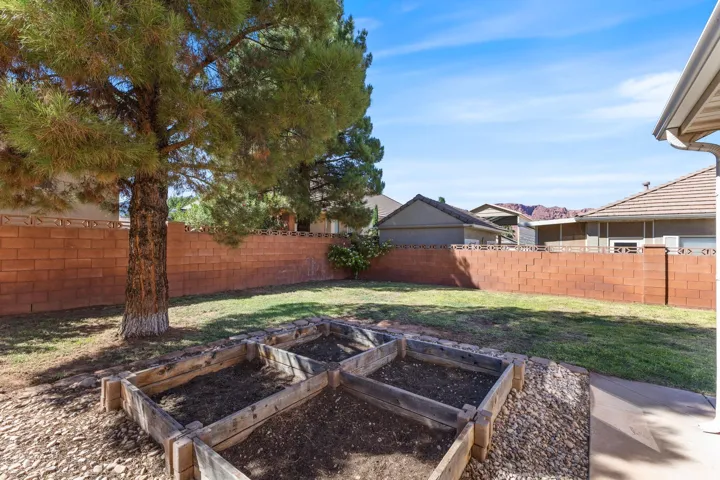 Expansive backyard featuring a mature tree, terraced garden beds, and a red brick privacy wall