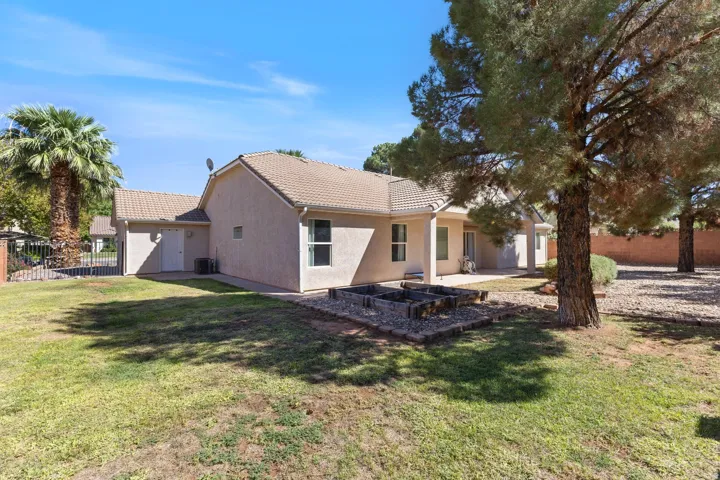 Expansive backyard featuring a grass lawn, mature trees, a concrete patio, and raised garden beds with stone borders