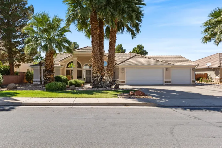 Stucco exterior with a tiled roof, mature palm trees, arched entryway, and a three-car garage